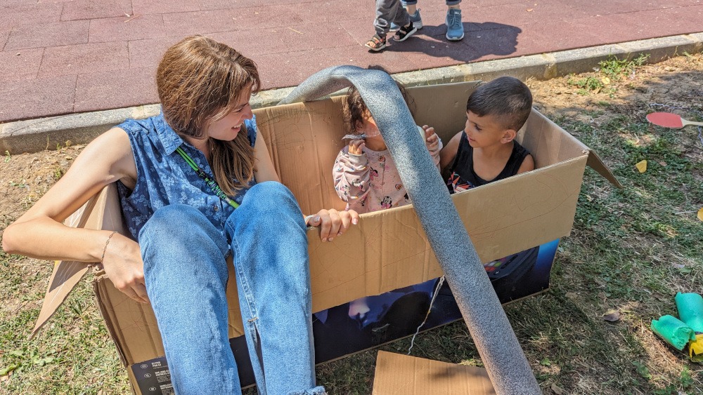 One adult, two children hang out in a box - Pop-Up Adventure Playground in Istanbul